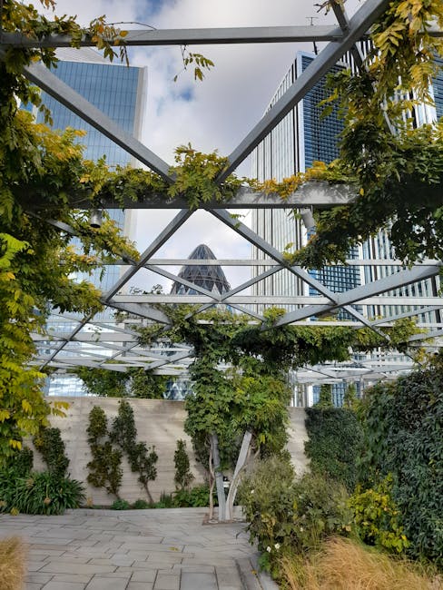 A pathway in a cultivated garden flanked by lush, well-maintained flowering shrubs and greenery on both sides, with a mix of blooming plants and trimmed foliage. The garden features a sandy-colored gr
